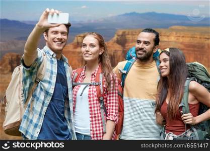 technology, travel, tourism, hike and people concept - group of smiling friends with backpacks taking selfie by smartphone over grand canyon national park background. friends with backpack taking selfie by smartphone. friends with backpack taking selfie by smartphone