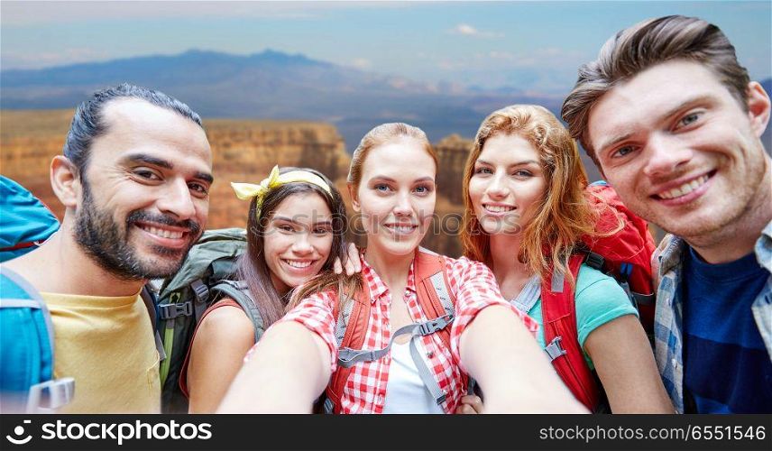 technology, travel, tourism, hike and people concept - group of smiling friends walking with backpacks taking selfie by smartphone or camera in woods. friends with backpack taking selfie in wood. friends with backpack taking selfie in wood