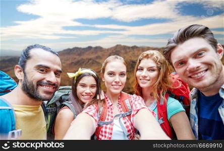 technology, travel, tourism, hike and people concept - group of smiling friends with backpacks taking selfie over grand canyon national park hills background. friends with backpack taking selfie ove mountains. friends with backpack taking selfie ove mountains