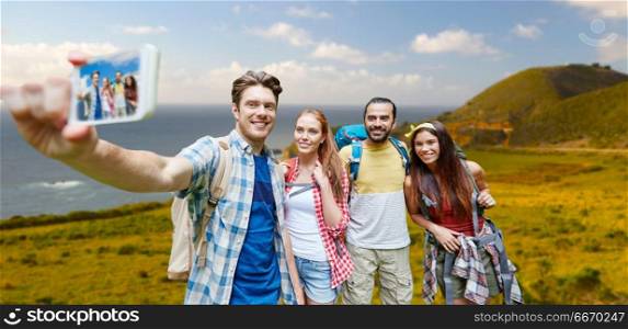 technology, travel, tourism, hike and people concept - group of smiling friends with backpacks taking selfie by smartphone over big sur coast of california background. friends with backpack taking selfie by smartphone. friends with backpack taking selfie by smartphone