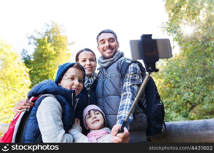 technology, travel, tourism, hike and people concept - happy family with backpacks taking picture by smartphone on selfie stick and hiking