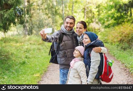 technology, travel, tourism, hike and people concept - happy family with backpacks taking selfie by smartphone and hiking