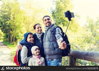technology, travel, tourism, hike and people concept - happy family with backpacks taking picture by smartphone on selfie stick and hiking. family with backpacks taking selfie and hiking