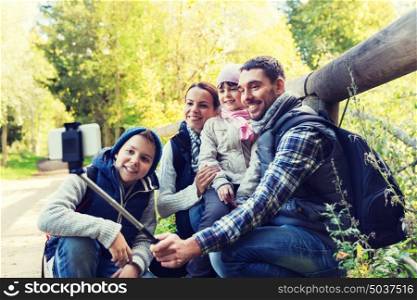 technology, travel, tourism, hike and people concept - happy family with backpacks taking picture by smartphone on selfie stick and hiking. family with backpacks taking selfie and hiking
