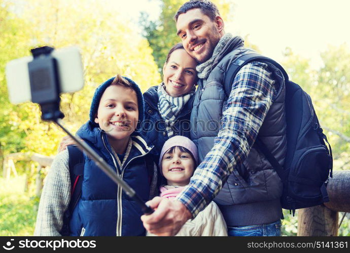 technology, travel, tourism, hike and people concept - happy family with backpacks taking picture by smartphone on selfie stick and hiking. family with backpacks taking selfie and hiking