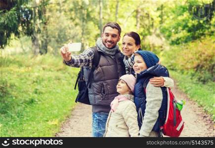 technology, travel, tourism, hike and people concept - happy family with backpacks taking selfie by smartphone and hiking. family with backpacks taking selfie by smartphone