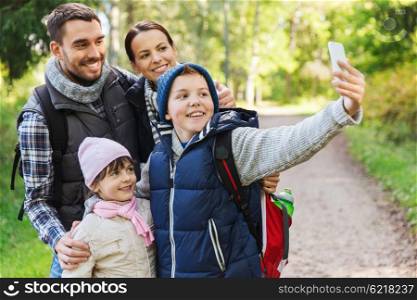 technology, travel, tourism, hike and people concept - happy family with backpacks taking selfie by smartphone and hiking