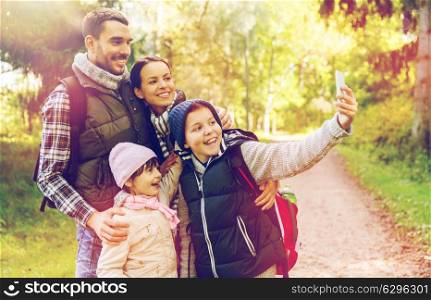 technology, travel, tourism, hike and people concept - happy family with backpacks taking selfie by smartphone and hiking. family with backpacks taking selfie by smartphone