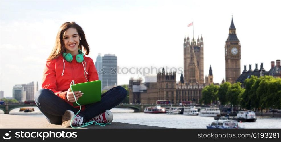 technology, travel, tourism, music and people concept - smiling young woman or teenage girl with tablet pc computer and headphones over london city and big ben tower background