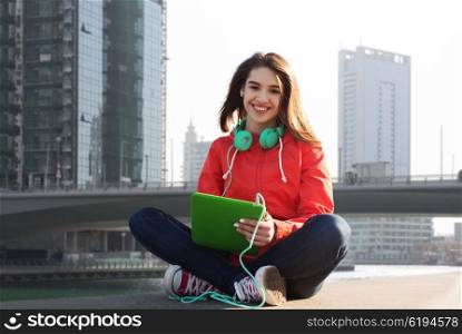 technology, travel, tourism, music and people concept - smiling young woman or teenage girl with tablet pc computer and headphones over dubai city street background
