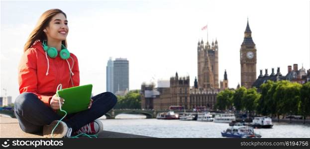 technology, travel, tourism, music and people concept - smiling young woman or teenage girl with tablet pc computer and headphones over london city and big ben tower background