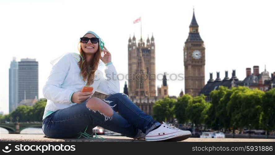 technology, travel, tourism, vacation and people concept - smiling young woman or teenage girl with smartphone and headphones listening to music over london city background