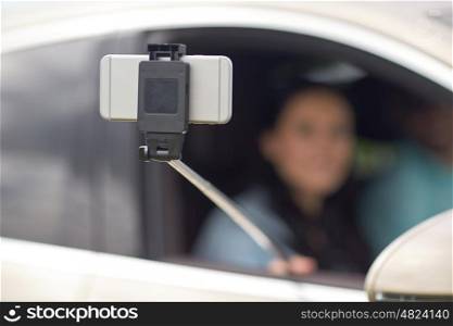 technology, travel, vacation, road trip and people concept - happy man and woman driving in car and taking selfie with smartphone