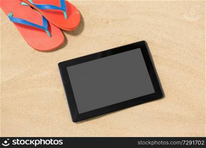 technology, vacation and summer holidays concept - tablet computer and flip flops on beach sand. tablet computer and flip flops on beach sand