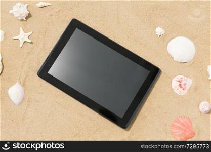technology, vacation and summer holidays concept - tablet computer and seashells on beach sand. tablet computer and seashells on beach sand