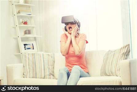 technology, virtual reality, cyberspace, entertainment and people concept - happy amazed young woman in virtual reality headset or 3d glasses and headphones sitting on sofa at home. woman in virtual reality headset or 3d glasses