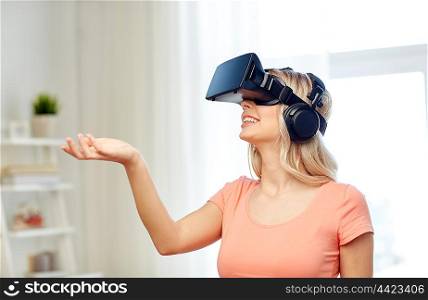 technology, virtual reality, entertainment and people concept - happy young woman in virtual reality headset or 3d glasses and headphones playing game at home and holding something invisible