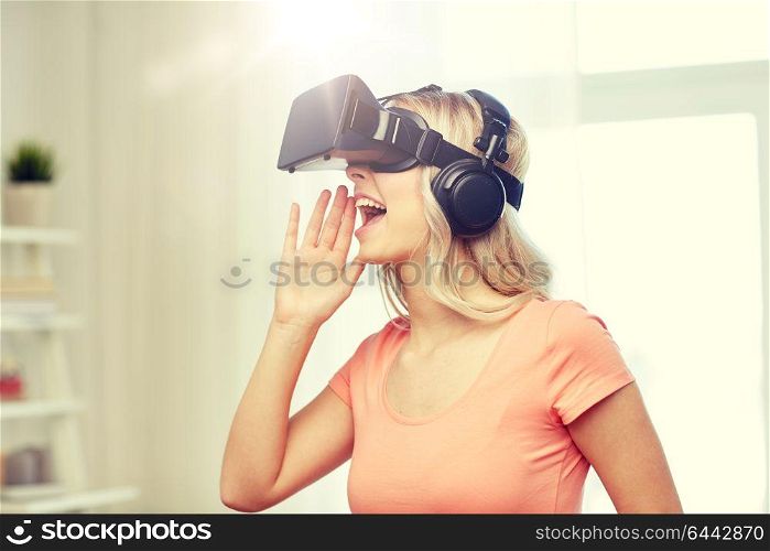 technology, virtual reality, entertainment and people concept - happy young woman in virtual reality headset or 3d glasses and headphones playing game at home and calling somebody out. woman in virtual reality headset or 3d glasses