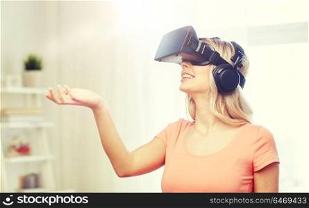 technology, virtual reality, entertainment and people concept - happy young woman in virtual reality headset or 3d glasses and headphones playing game at home and holding something invisible. woman in virtual reality headset or 3d glasses
