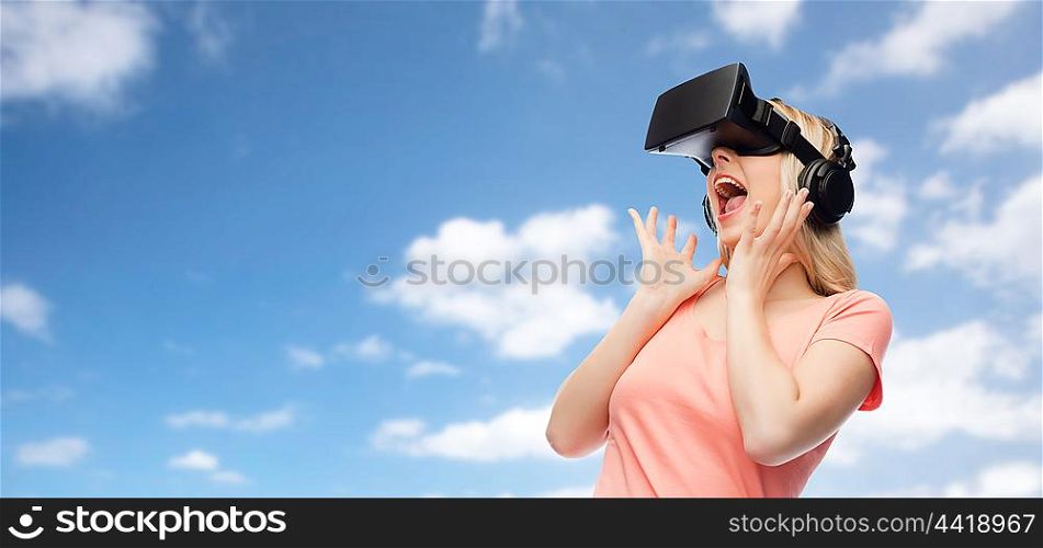 technology, virtual reality, entertainment and people concept - happy young woman with virtual reality headset or 3d glasses and headphones over blue sky and clouds background