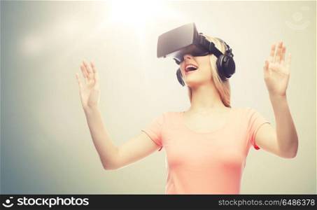 technology, virtual reality, entertainment and people concept - happy young woman with virtual reality headset or 3d glasses and headphones playing game over gray background. woman in virtual reality headset or 3d glasses. woman in virtual reality headset or 3d glasses