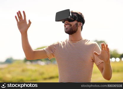 technology, virtual reality, entertainment and people concept - smiling man with vr headset or 3d glasses playing video game outdoors. smiling man in virtual reality headset outdoors