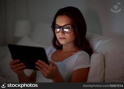 technology, vision, communication and people concept - young woman in glasses with tablet pc computer in bed at home bedroom at night. woman with glasses and tablet pc in bed at home