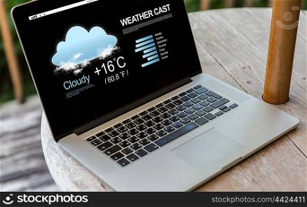 technology, weather cast, business and modern life concept- close up of open laptop computer with meteo forecast on screen on table at hotel terrace