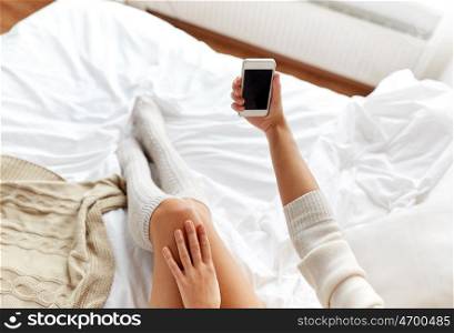 technology, winter, augmented rality and people concept - young woman in bed holding smartphone with black empty screen at home bedroom