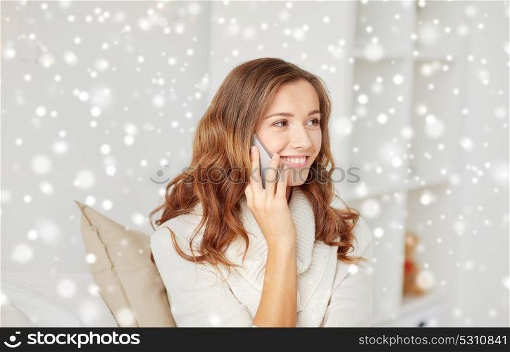 technology, winter, communication and people concept - happy young woman calling on smartphone at home over snow. happy young woman calling on smartphone at home