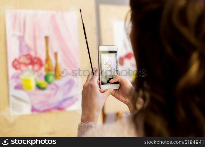 technologyl, creativity and people concept - woman artist or student with smartphone and brush photographing still life painting or picture at art school studio. woman with painting on smartphone at art school