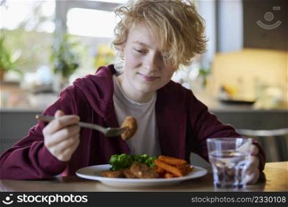 Teeange Girl Eating Vegan Meal Sitting At Table In Kitchen At Home