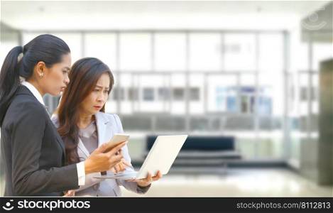 teen age worker holding mobile phone in hand talk to senior worker working with laptop while the woman serious about inter net can not be connected