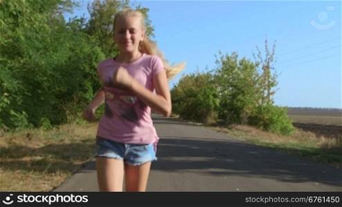 Teen blonde girl running along country road looking at the camera