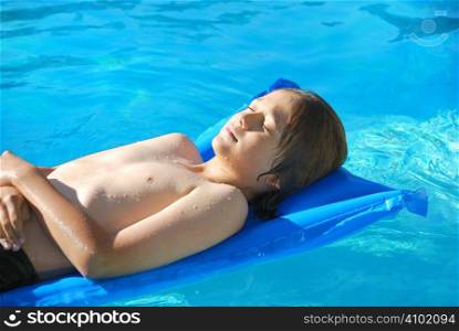 Teen boy lying wet on an air mattress in the pool on a sunny day.