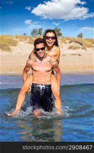 Teen couple running piggyback on summer beach splashing water