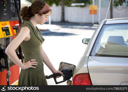 Teen girl at the gas station filling up the fuel tank in her gas efficient car.