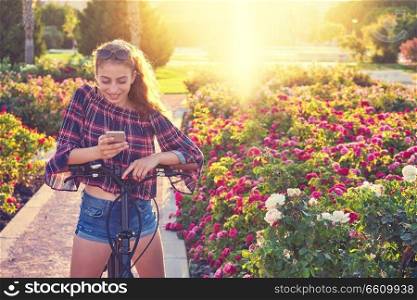 Teen girl bicycle playing with smartphone in a city flowers park