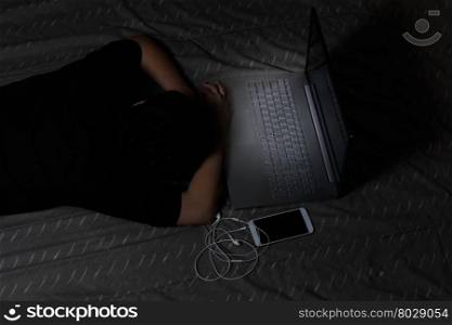 Teen girl falls asleep with her computer still on while in bed. Light effect on computer keyboard.