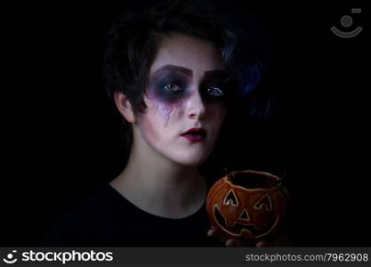 Teen girl in scary makeup holding pumpkin container on black background. Trick or treat concept.