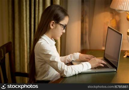 Teen girl in school uniform sitting behind table and using laptop at cabinet