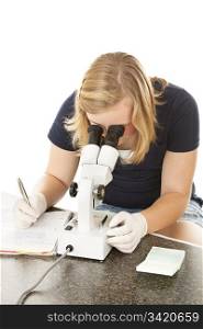 Teen girl in science class looks through microscope and writes down her observations. White background.