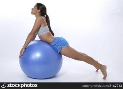 Teen girl in workout clothes stretching over exercise ball.