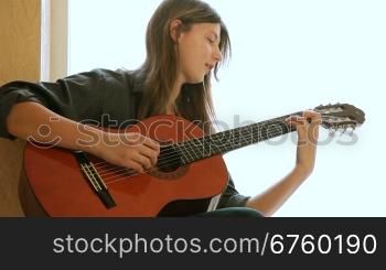 Teen girl learning to play guitar at home. Medium shot