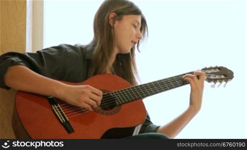 Teen girl learning to play guitar at home. Medium shot