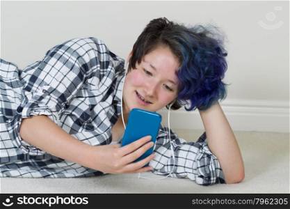 Teen girl looking at cell phone while lying down listening to music at home. Layout in horizontal format.