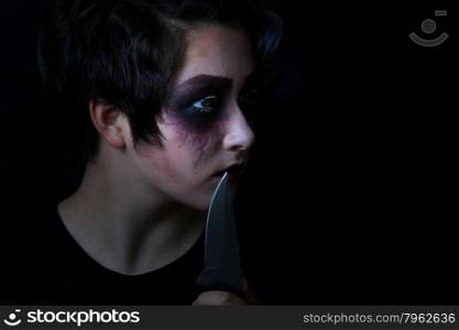Teen girl masked in scary makeup with combat knife on black background.