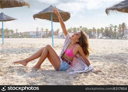 Teen girl on the beach happy pointing finger to sky near thatch umbrellas