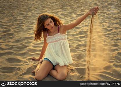 Teen girl on the beach playing with sand in the wind
