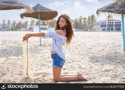 Teen girl on the beach playing with sand near thatch umbrellas